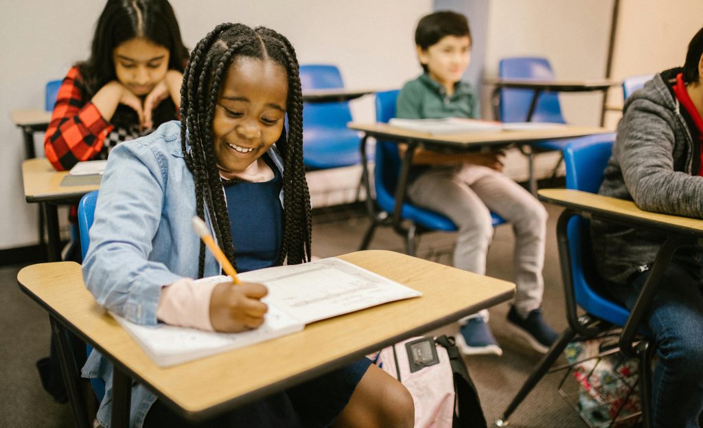 A diverse class of children, with a Black student laughing while working.